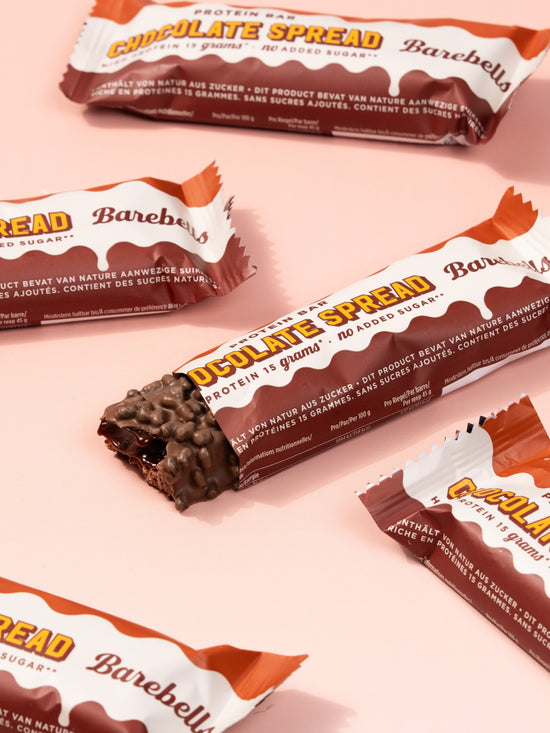 Multiple Barebells Chocolate Spread bars with orange and white wrappers arranged on pink background