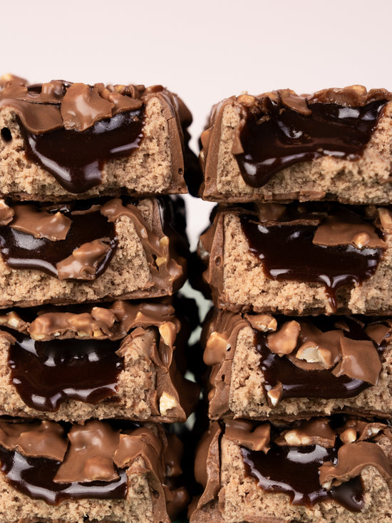 Two stacks of Barebells Hazelnut Spread bars with white and green packaging, showing chocolate-coated exterior with visible hazelnut pieces